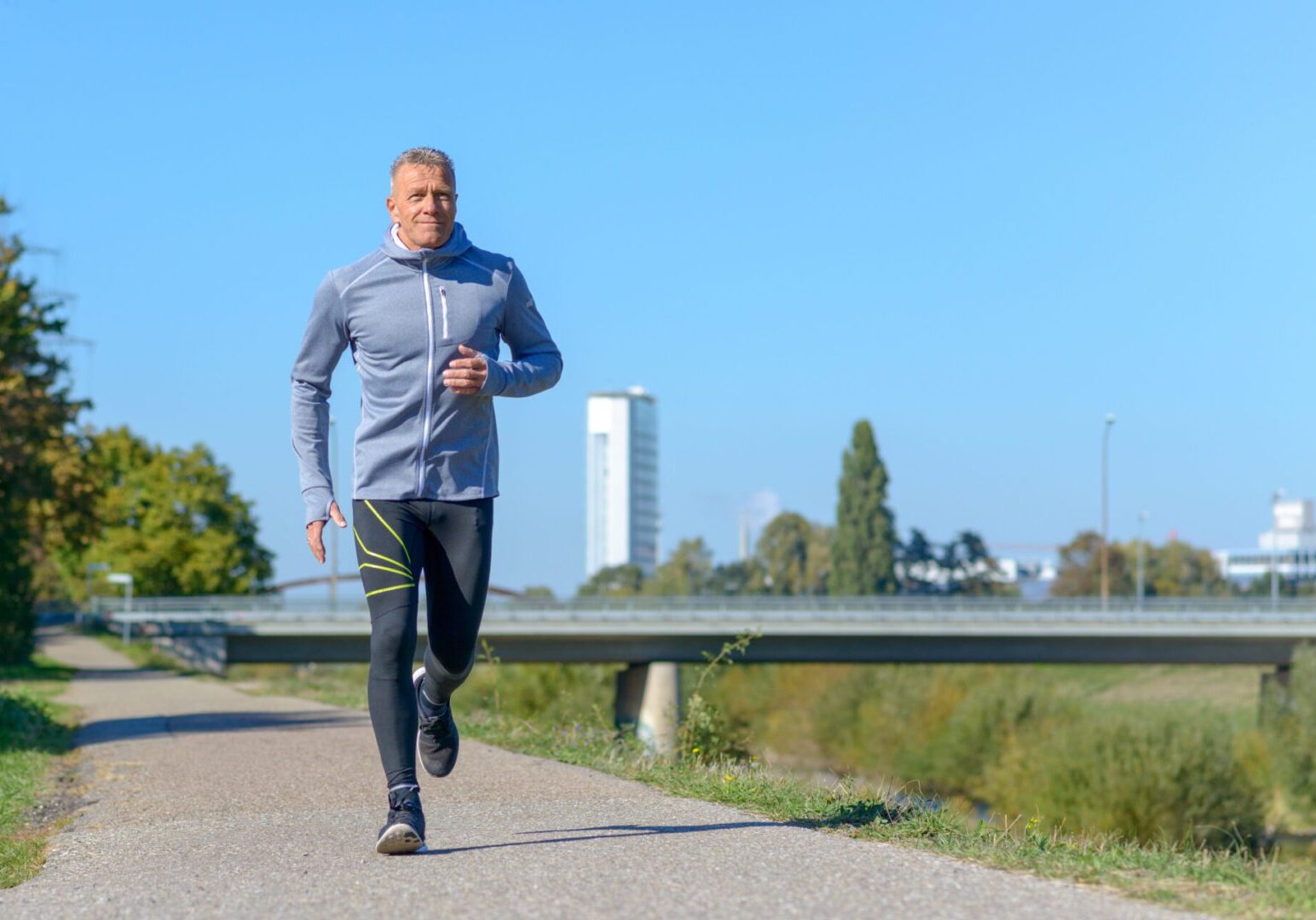 Middle-aged man jogging along alley in park on sunny day